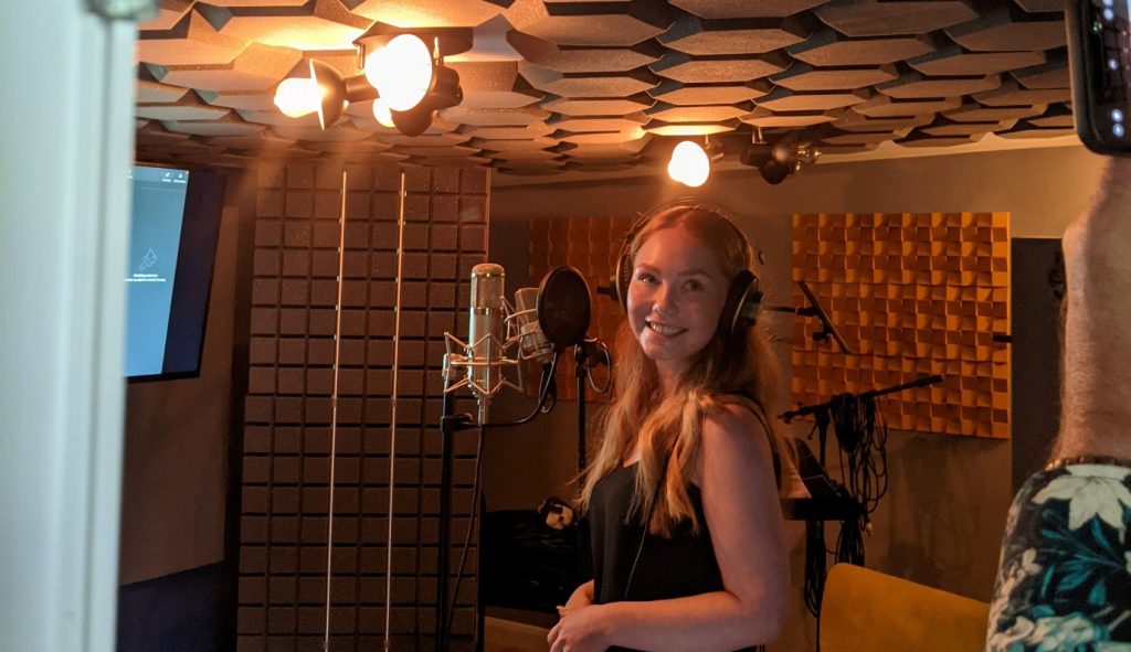 A young woman wearing headphones smiles in a recording studio